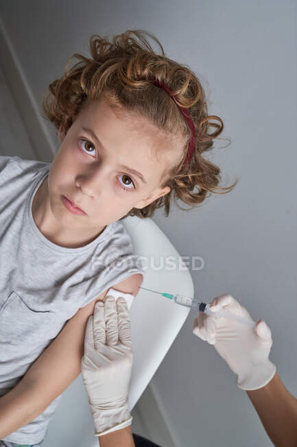 Unrecognizable crop doctor in latex gloves filling in syringe with vaccine  medication from bottle preparing for injection in shoulder of boy with  curly hair — people, from above - Stock Photo | #445808514