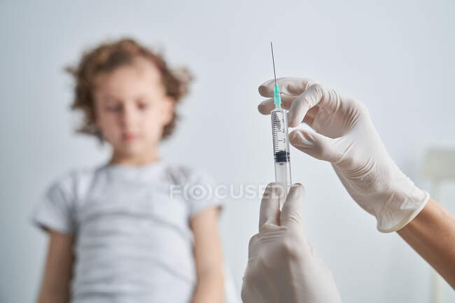 Crop hand in latex glove of anonymous doctor demonstrating syringe with vaccine medication before giving injection to boy — Stock Photo