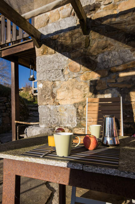 Copos brancos e cafeteira quente colocados na mesa com torrada quente e copo de suco de laranja fresco na varanda ao ar livre com montanha no fundo — Fotografia de Stock