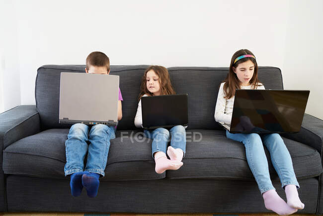 Gruppe von Kindern benutzt Laptops, während sie zu Hause auf dem Sofa sitzen — Stockfoto