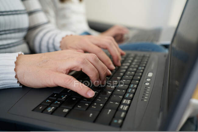 Vista lateral de la mujer anónima en ropa casual escribiendo en el teclado del ordenador portátil mientras trabaja en el trabajo independiente en casa - foto de stock