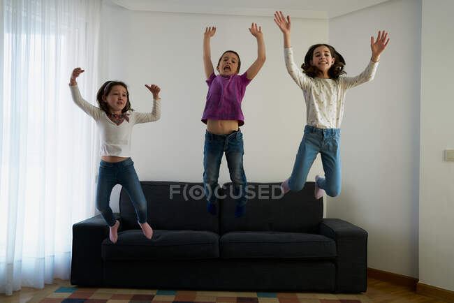 Group of cheerful kids jumping from sofa in living room — Stock Photo