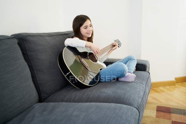 Jovem aprendendo irmã a tocar guitarra no sofá em casa — Fotografia de Stock