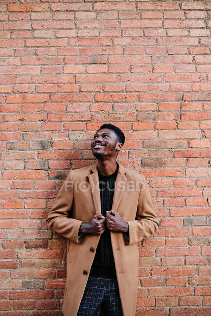Moderne fröhliche erwachsene schwarze Afroamerikaner tragen stylische Kleidung und schauen weg, während sie vor einer Ziegelsteinmauer stehen — Stockfoto