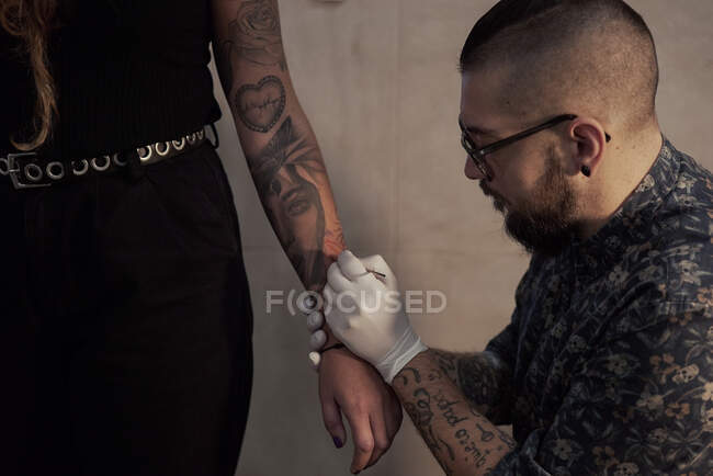Alto angolo di tatuaggio maschile che fa tatuaggio a mano libera e schizzo di disegno sul braccio del cliente del raccolto nel salone — Foto stock
