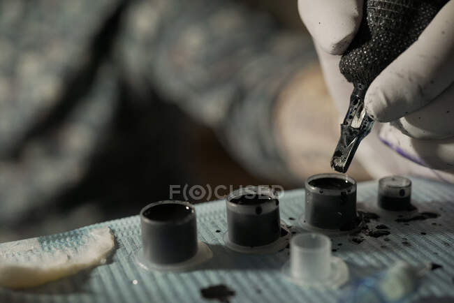 Closeup de cultura tatuador irreconhecível mergulhando máquina de tatuagem em tinta preta enquanto trabalhava no salão — Fotografia de Stock