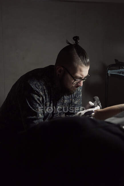Татуировщик с помощью машины и сделать татуировку с черными чернилами в салоне в анонимном обрезанном клиенте — стоковое фото