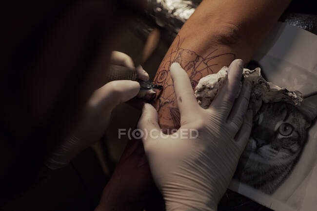 Зверху невизначений чоловічий татуювач використовує машину та робить татуювання на руці клієнта в салоні — стокове фото