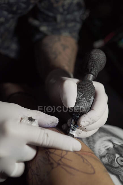 Зверху невизначений чоловічий татуювач використовує машину та робить татуювання на руці клієнта в салоні — стокове фото