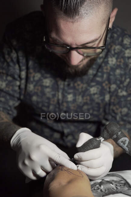 Tätowierer mit Maschine und Herstellung von Tätowierungen mit schwarzer Tinte im Salon in anonym zugeschnittenen Kunden — Stockfoto