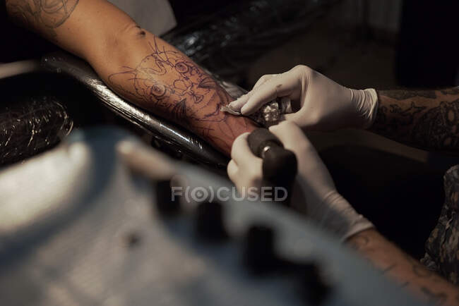 De cima de tatuador masculino irreconhecível usando máquina e fazendo tatuagem no braço do cliente de colheita no salão — Fotografia de Stock