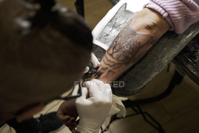 Сверху неузнаваемый мужчина-татуировщик, использующий машину и делающий татуировку на руке клиента в салоне — стоковое фото