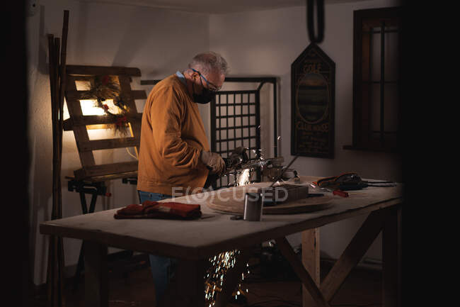 Мужчина в защитных перчатках и маске с помощью сварочной машины во время работы в темной мастерской — стоковое фото