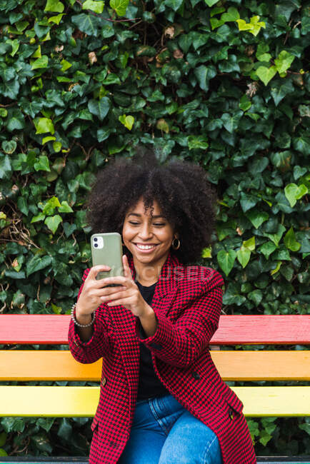 Задоволена афро-американська жінка сидить на лавці в місті і робить автопортрет на смартфоні — стокове фото