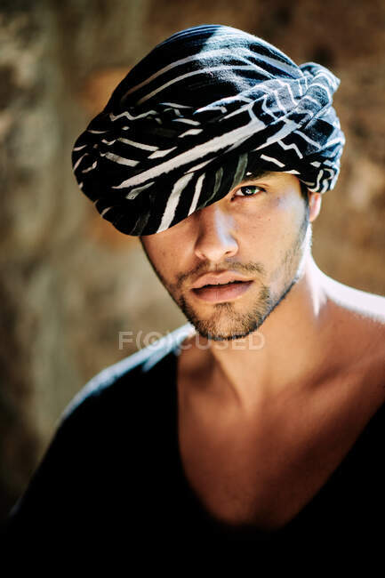 Молодой чувственный красивый арабский мужчина с тюрбановой моделью в стильной хипстерской летней одежде, смотрящий в камеру, стоя на улице — стоковое фото