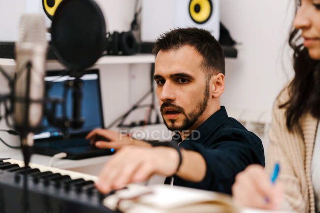 Músico masculino tocando sintetizador e cantando junto com a mulher durante a gravação da música em casa — Fotografia de Stock