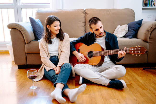 Романтична пара сидить на підлозі вдома з келихом винограду і грає на акустичній гітарі вдома — стокове фото