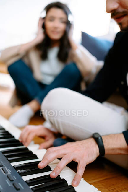 Homem tocando sintetizador e mulher ouvindo música em fones de ouvido enquanto sentado no chão em casa e gravando nova música — Fotografia de Stock