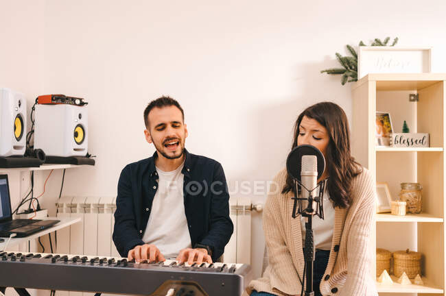 Männlicher Musiker spielt Synthesizer und singt zusammen mit Frau, während er zu Hause Songs aufnimmt — Stockfoto