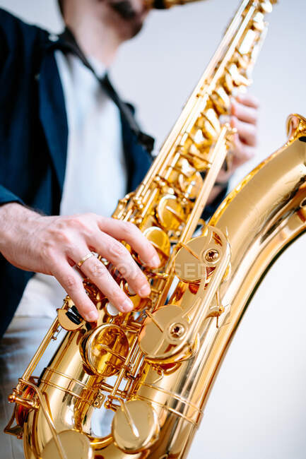 Crop músico masculino tocando saxofone enquanto estava de pé no fundo branco e olhando para longe — Fotografia de Stock