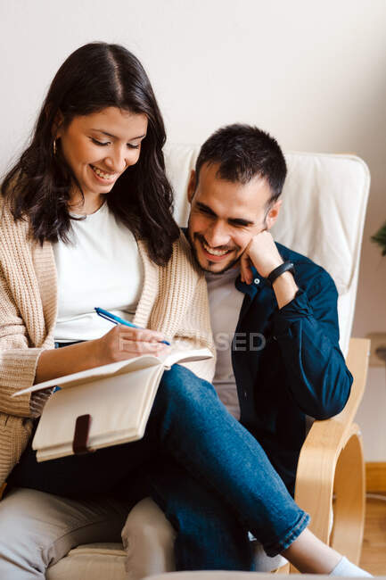 Content couple of musicians sitting together in armchair and taking notes while composing music at home — Stock Photo