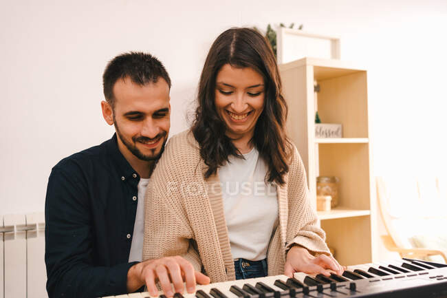 Мужчина-музыкант играет на синтезаторе и поет вместе с женщиной во время записи песни дома — стоковое фото