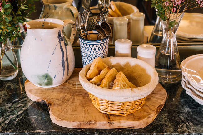 High angle of pieces of fresh bread in basket placed on table with various tableware prepared for buffet breakfast — Stock Photo