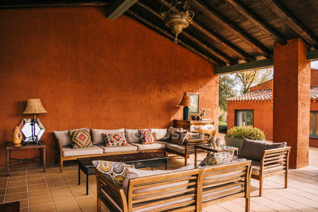 Canapés confortables et table placés sur la terrasse sous le toit en bois du chalet en été — Photo de stock