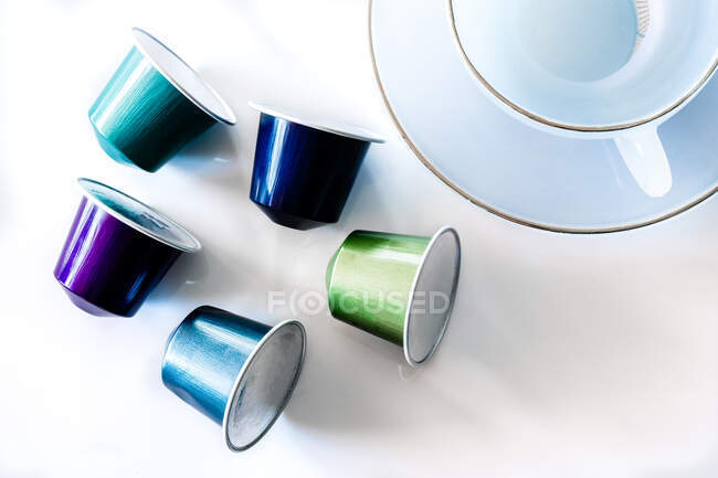 Vista dall'alto della collezione di cialde di caffè posizionate vicino a tazza e piattino in ceramica vuota su sfondo bianco — Foto stock