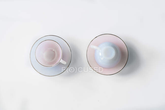 Vista superior de tazas y platillos vacíos de cerámica colocados sobre fondo blanco en el estudio - foto de stock