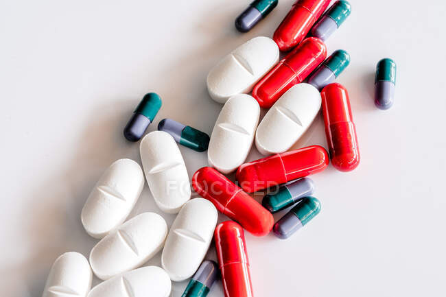 Вид зверху на різнокольорові і білі таблетки і капсули, розміщені на білому столі — стокове фото