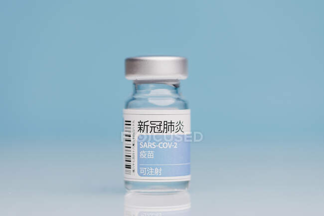 Flacon en verre avec vaccin de COVID 19 placé sur la table sur fond bleu — Photo de stock