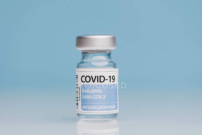 Frasco para injetáveis de vidro com a vacina COVID 19 colocada na mesa sobre fundo azul — Fotografia de Stock