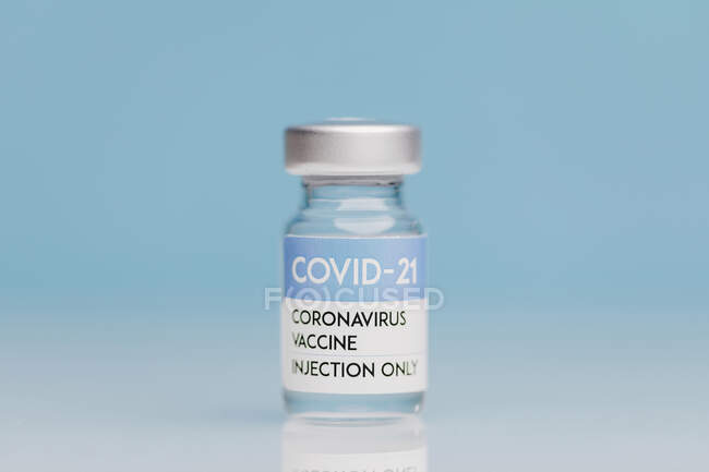 Flacon en verre avec vaccin de COVID 19 placé sur la table sur fond bleu — Photo de stock