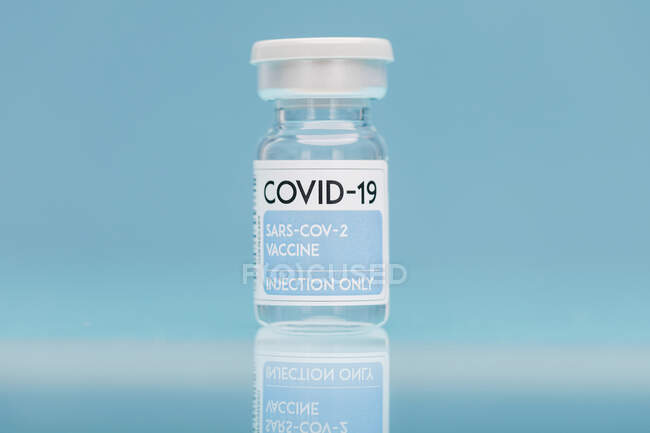 Flaconcino di vetro con vaccino di COVID 19 posto sul tavolo su fondo blu — Foto stock