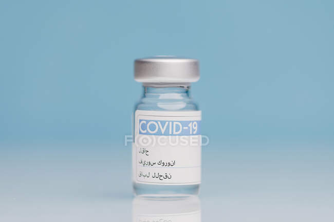 Flaconcino di vetro con vaccino di COVID 19 posto sul tavolo su fondo blu — Foto stock