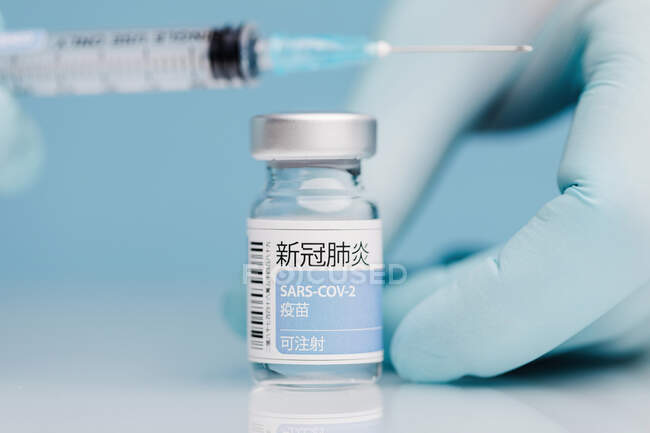 Fechamento de um médico irreconhecível nas luvas que enche a seringa com a vacina contra o coronavírus em frasco de vidro sobre fundo azul — Fotografia de Stock