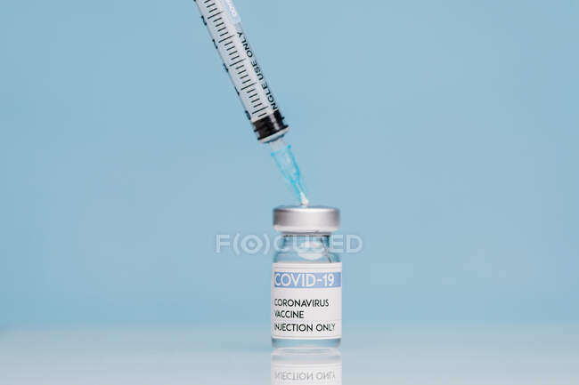 Medizinische Spritze und Glasflasche mit Coronavirus-Impfstoff vor blauem Hintergrund — Stockfoto