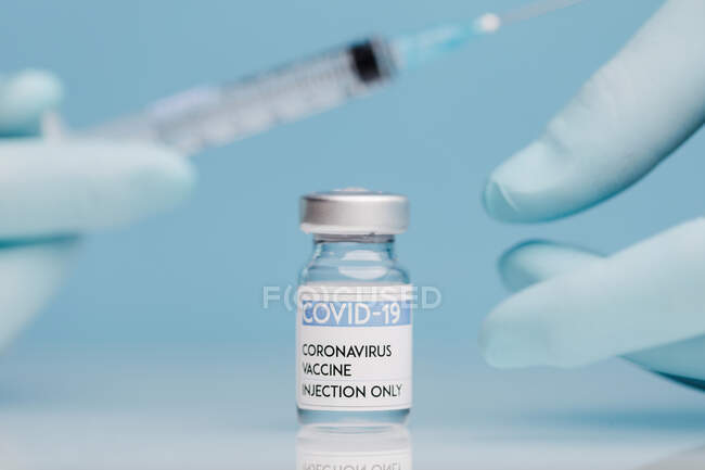 Closeup of crop unrecognizable doctor in gloves filling syringe with vaccine from coronavirus in glass vial on blue background — Stock Photo