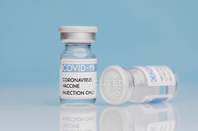 Flacons en verre avec vaccin de COVID 19 placés sur la table sur fond bleu — Photo de stock