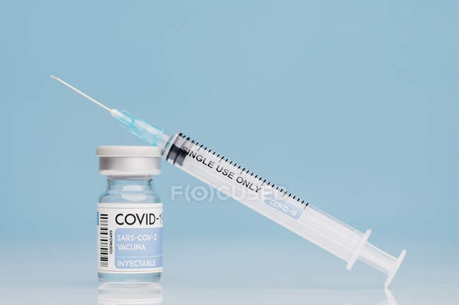 Медичний шприц і скляний флакон з коронавірусною вакциною проти синього фону. — стокове фото