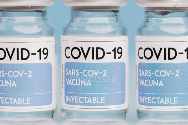 Flacons en verre avec vaccin de COVID 19 placés sur la table en rangée sur fond bleu — Photo de stock