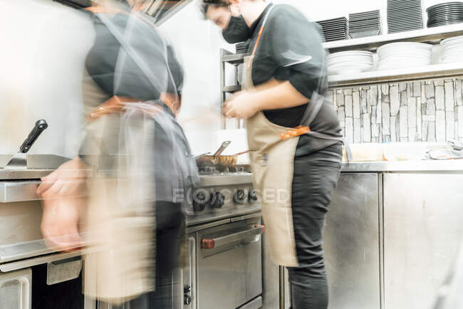 Размытые неузнаваемые повара готовят еду, работая вместе на профессиональной кухне — стоковое фото