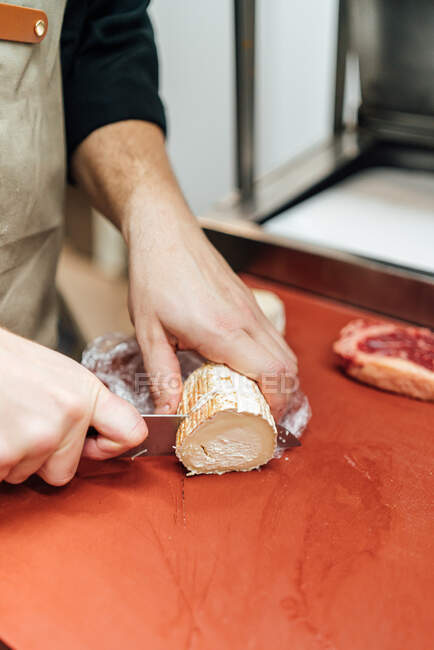 Crop faceless shot of person cutting goat cheese in a restaurant kitchen — Stock Photo