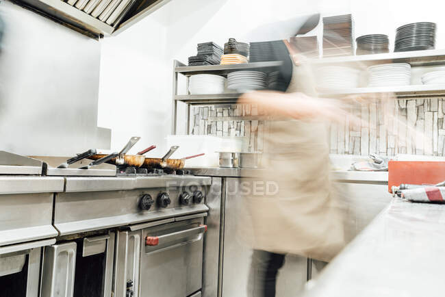 Cuisinier flou méconnaissable préparant des aliments tout en travaillant dans une cuisine professionnelle — Photo de stock