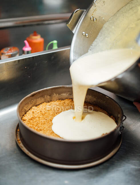 Cropped unrecognizable cook pouring cream on cake tin while preparing delicious cheesecake dessert in cafe — Stock Photo
