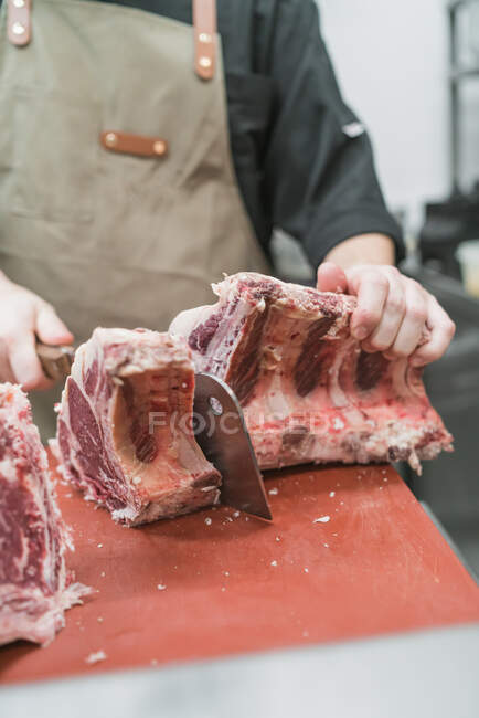 Обрізати невпізнаваний чоловічий м'ясник у фартухах нарізати м'ясо гострим ножем під час роботи на кухні — стокове фото