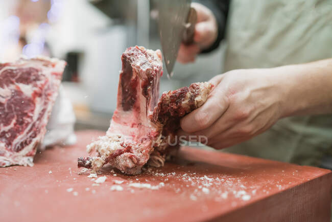Ernte bis zur Unkenntlichkeit männlicher Metzger in Schürze schneidet Fleisch mit scharfem Messer während der Arbeit in der Küche — Stockfoto
