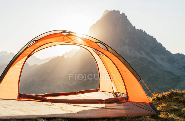 Tienda de campaña moderna situada en la colina en el terreno de las tierras altas en el fondo de la salida del sol en las montañas de los Pirineos - foto de stock