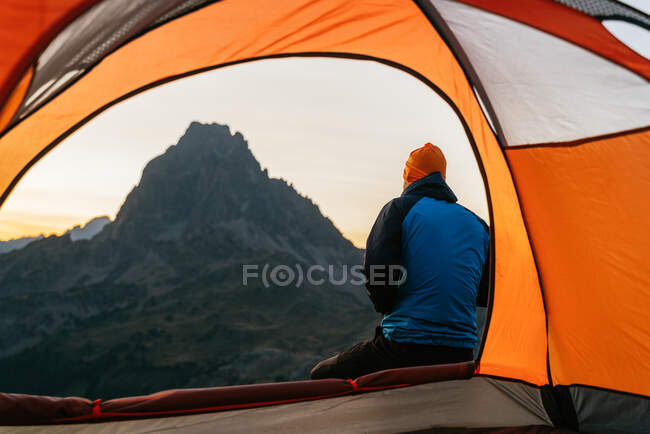 Back view of unrecognizable hiker sitting on hill near tent admiring view of scenic Pyrenees mountain range in morning — Stock Photo